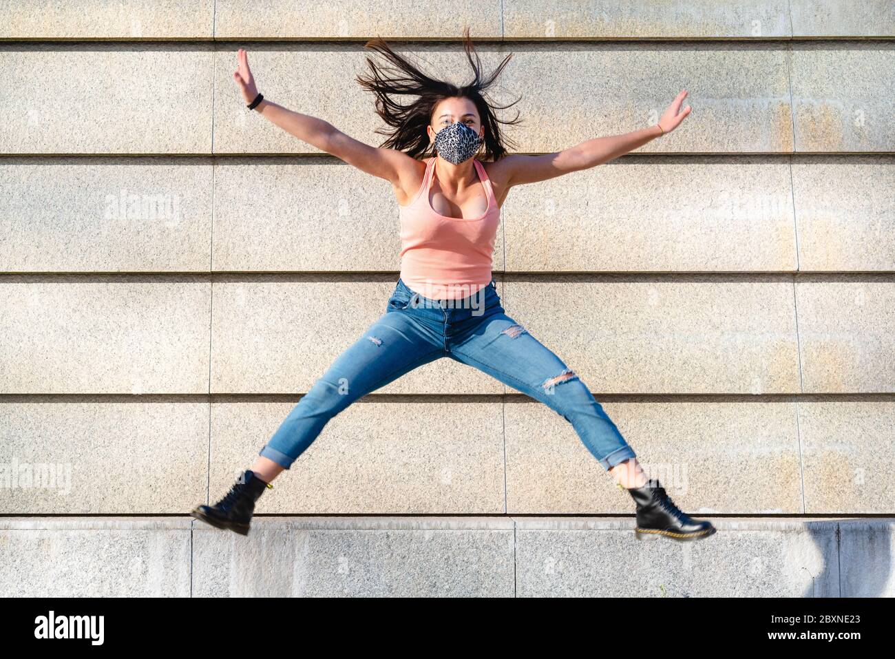 Giovane ragazza della generazione Z che indossa una maschera leopardo fa un salto acrobatico con gambe aperte, concetto di pensiero positivo e ottimismo Foto Stock