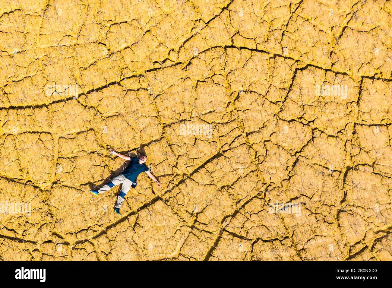 Uomo sdraiato su una terra crackizzata dalla siccità. Foto Stock