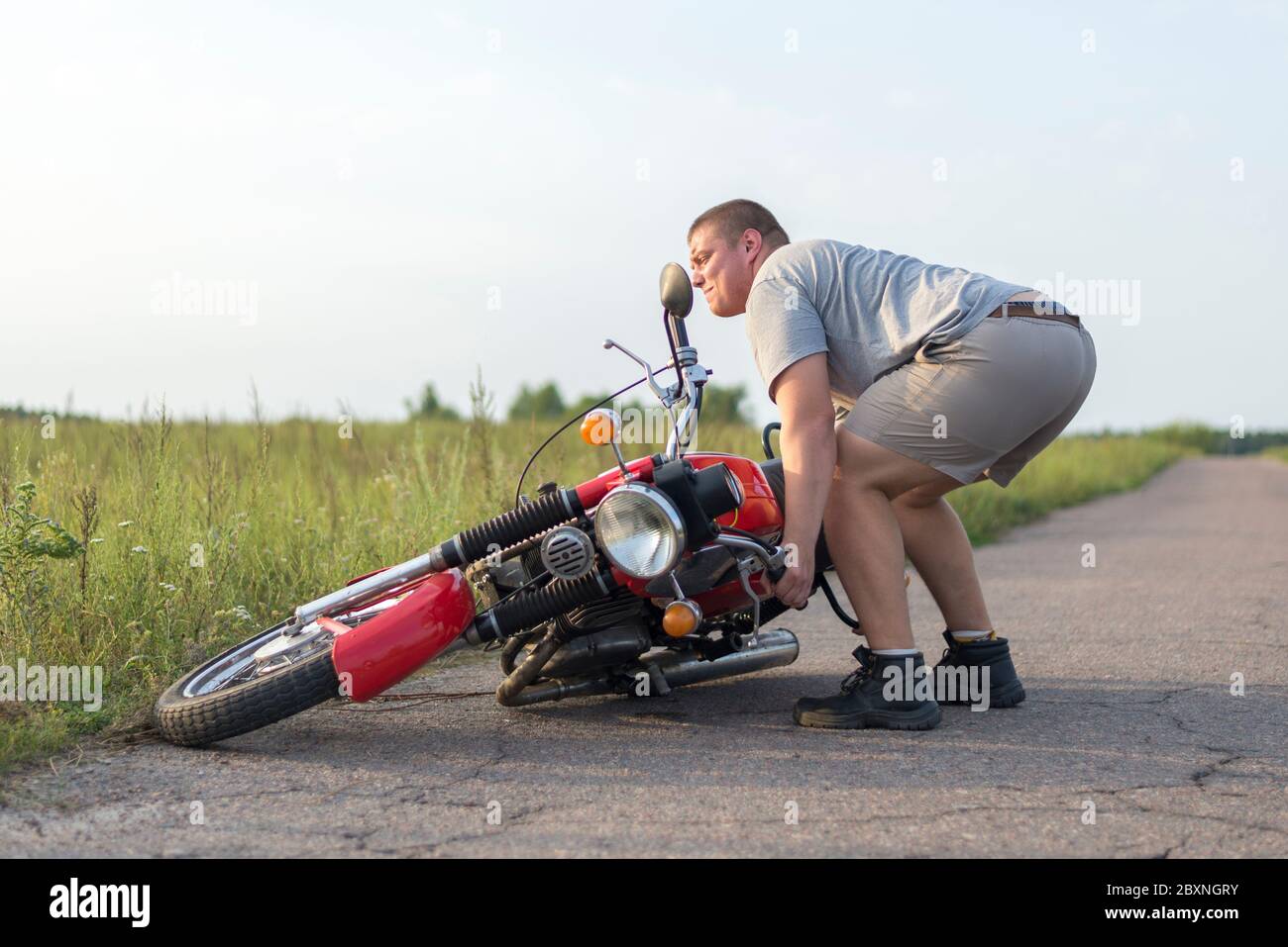 Un uomo solleva una motocicletta pesante che è caduta dopo un incidente Foto Stock
