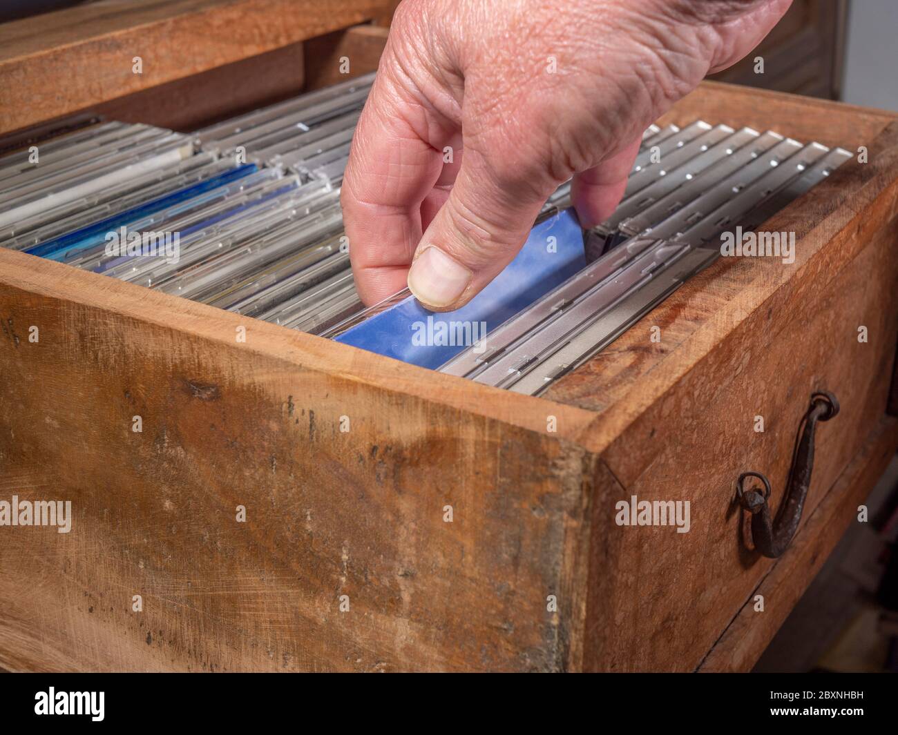 Una mano di un uomo che controlla i CD di una collezione in un vecchio cassetto di legno e ne seleziona uno da estrarre. Foto Stock