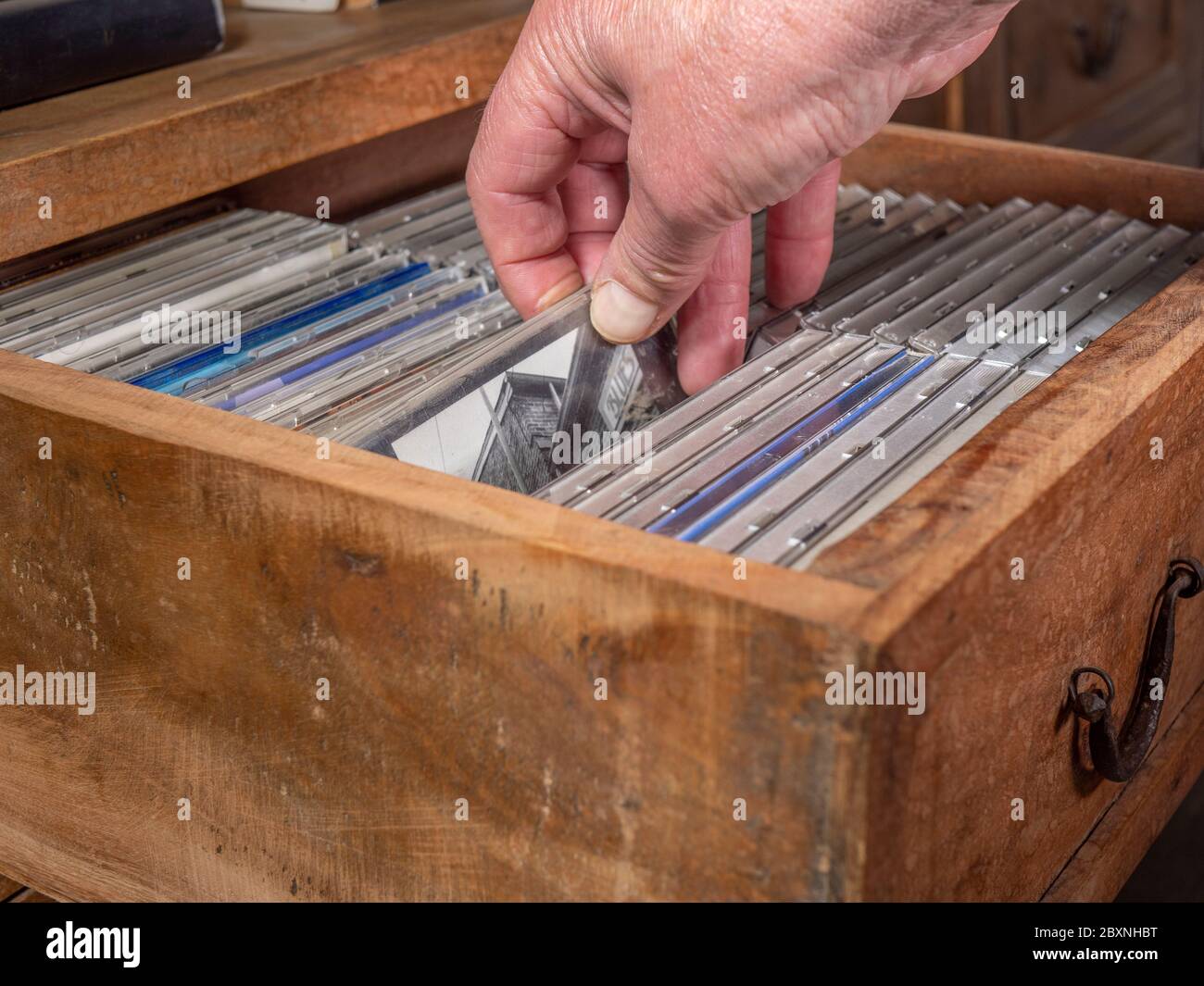Una mano di un uomo che controlla i CD di una collezione in un vecchio cassetto di legno e ne seleziona uno da estrarre. Foto Stock