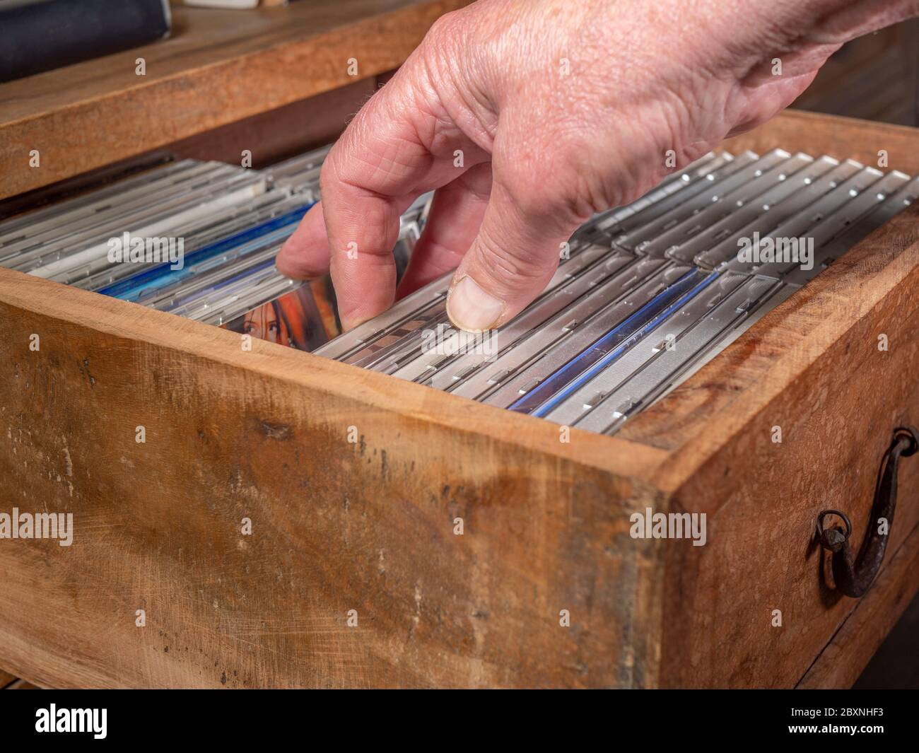 Una mano di un uomo che controlla i CD di una collezione in un vecchio cassetto di legno e ne seleziona uno da estrarre. Foto Stock