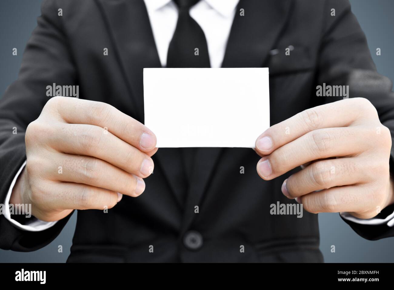 Primo piano di uomo d'affari che mostra un pezzo di carta bianco in abito nero. Idea per carta di credito o carta di visita. Foto Stock