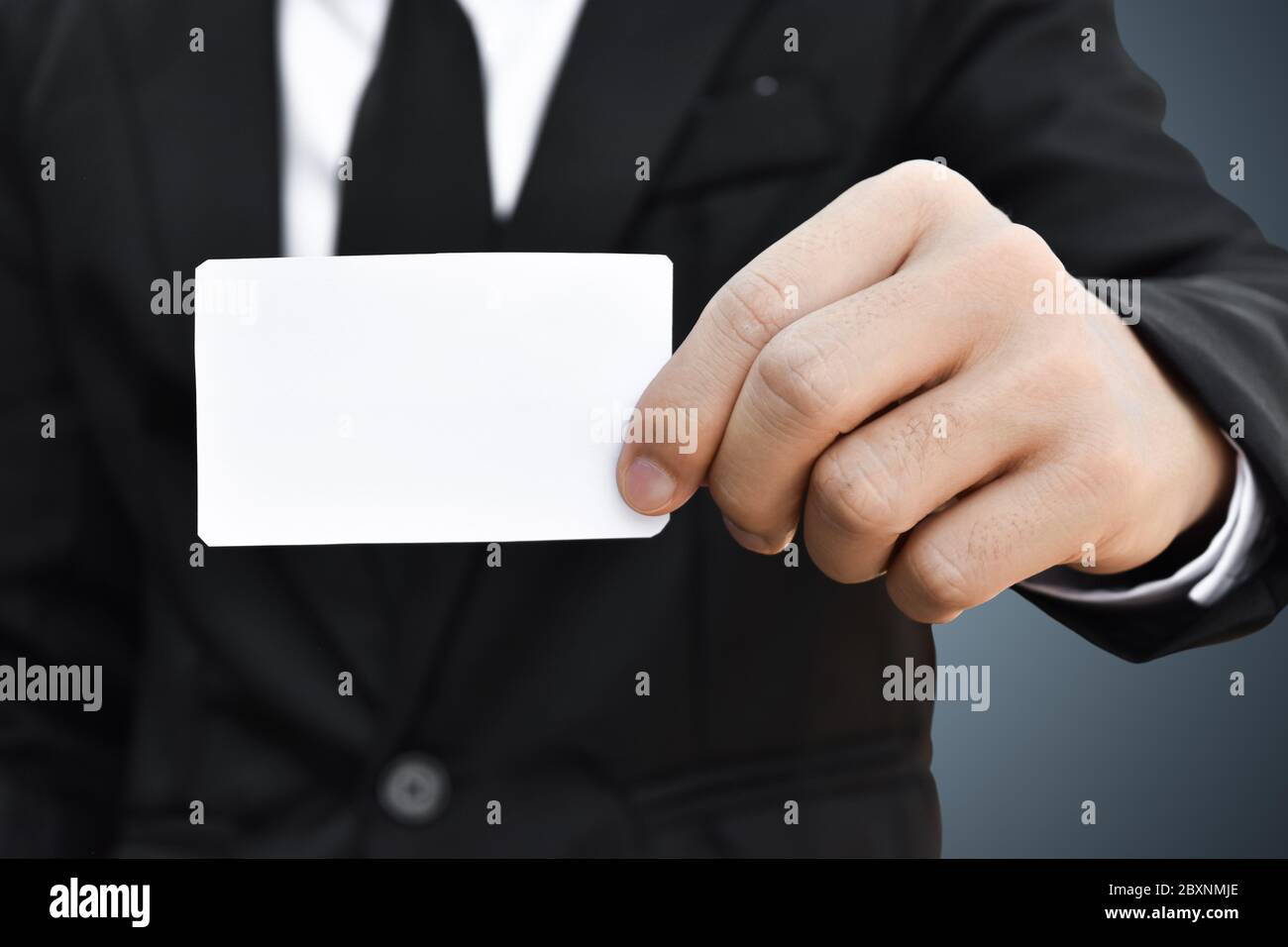 Primo piano di uomo d'affari che mostra un pezzo di carta bianco in abito nero. Idea per carta di credito o carta di visita. Foto Stock