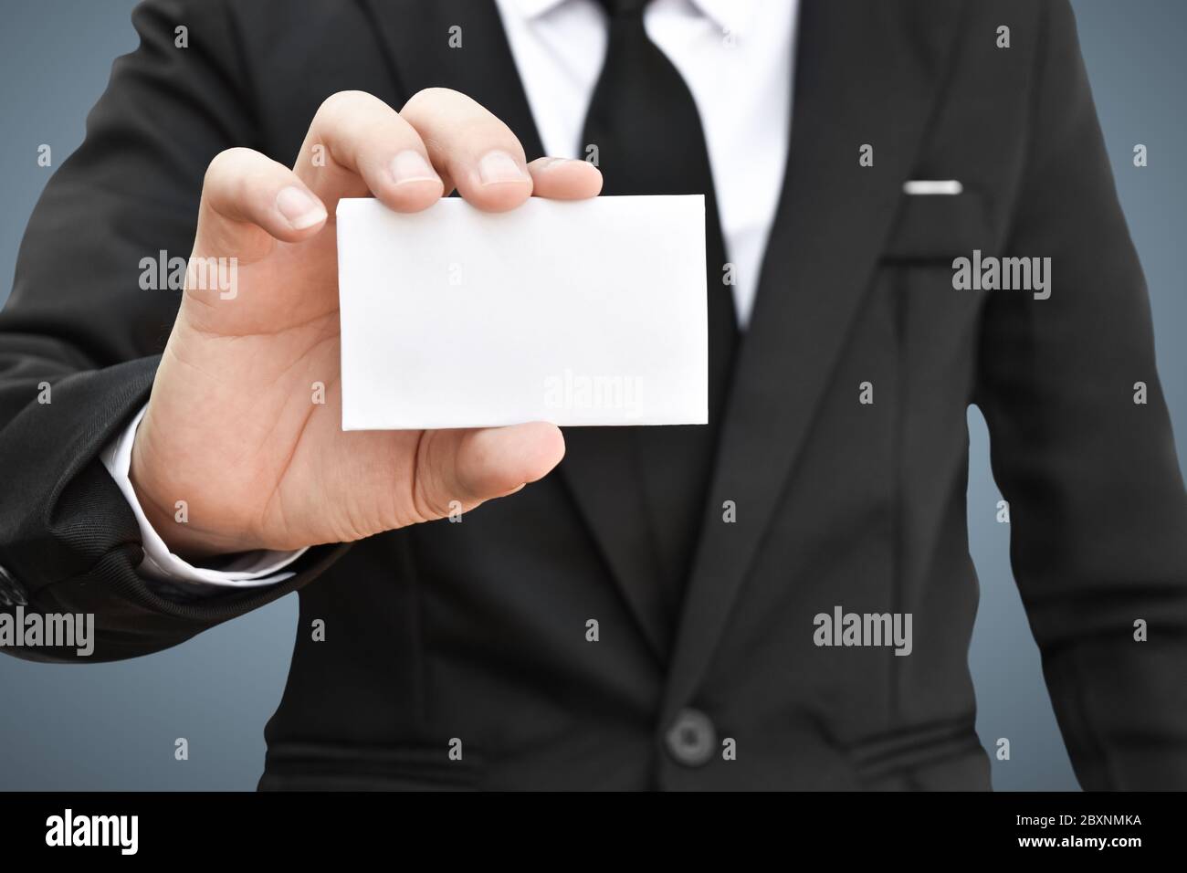 Uomo d'affari che mostra un pezzo di carta bianco in abito nero. Idea per carta di credito o carta di visita. Foto Stock
