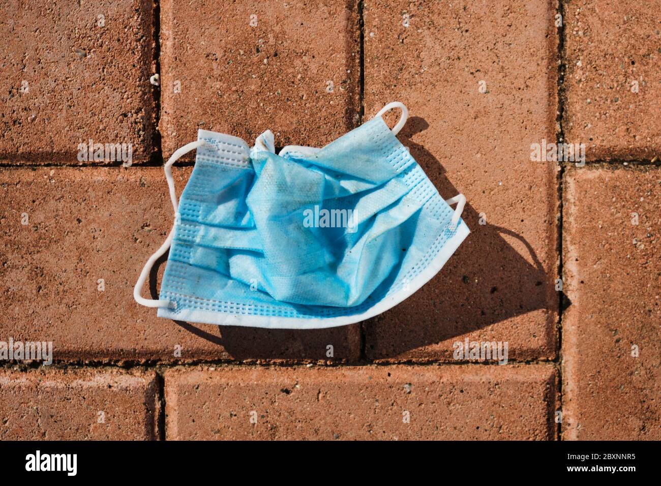 vista ad alto angolo di una maschera chirurgica blu utilizzata gettata sul marciapiede di una strada cittadina Foto Stock