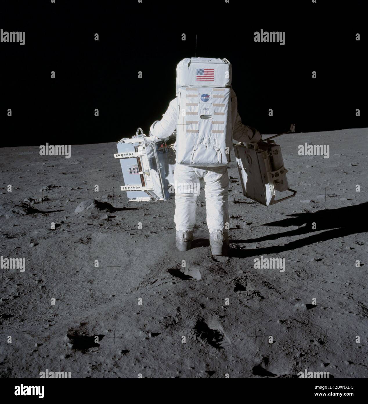 AS11-40-5942 - Apollo 11 - immagine della missione Apollo 11 - l'astronauta Edwin Aldrin porta esperimenti nell'area di implementazione; ambito e contenuto: Il database originale descrive questo come: Descrizione: L'astronauta Edwin E. Aldrin, pilota del modulo Lunar (LM), trasporta il pacchetto di esperimenti sismici passivi (PSEP) (a sinistra) e il laser Ranging Retrorefector (LRRR) (a destra), nell'area di implementazione. Questi due esperimenti costituiscono il pacchetto sperimentale scientifico Early Apollo (EASEP). Immagine presa alla base della tranquillità durante la missione Apollo 11. La rivista originale è stata etichettata S. Film Type: EKTACHROME EF SO168 c. Foto Stock