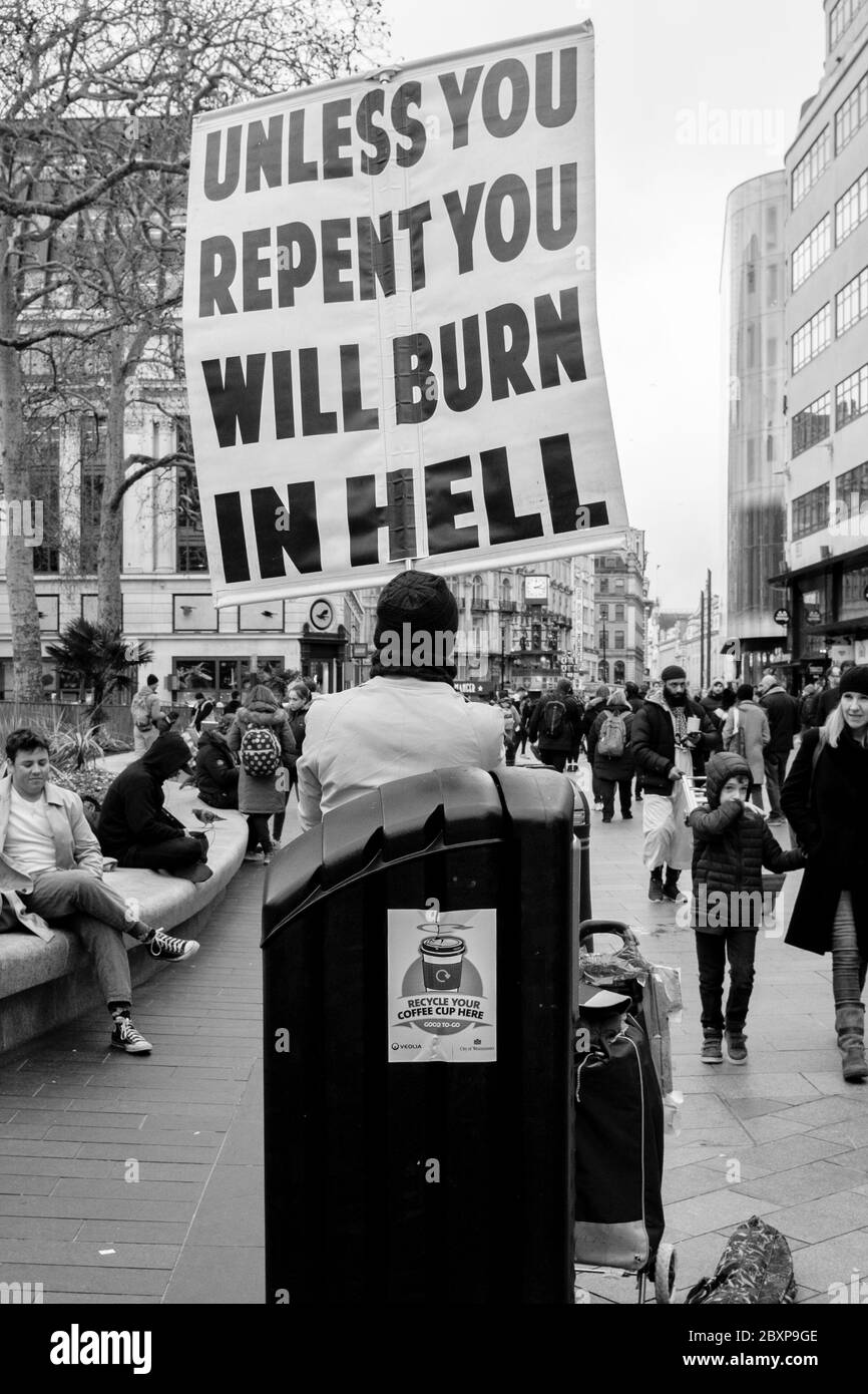 Fotografia di strada bianca e nera a Londra: Attivista religioso con placard accanto al cestino per il riciclaggio delle tazze di caffè. Foto Stock