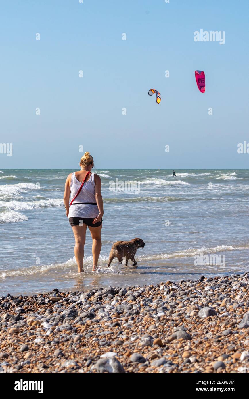 Vista posteriore di donna che cammina il suo cane sul Seashore. Kite Surfers sono in background Foto Stock