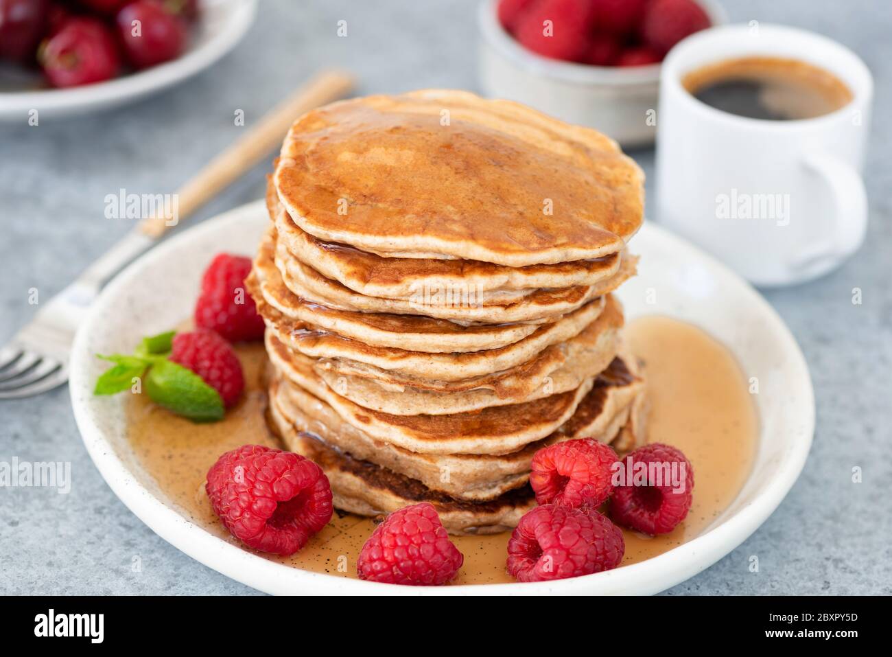 Pancake con sciroppo e lamponi su piatto, tazza di caffè espresso sullo sfondo. Gustosi piatti dolci per la colazione Foto Stock