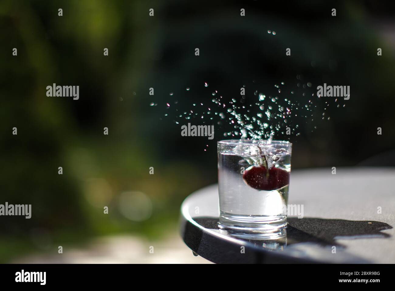 Ciliegia rossa che cade in un bicchiere d'acqua producendo spruzzi d'acqua, congelare nel tempo foto, concettuale. Foto Stock