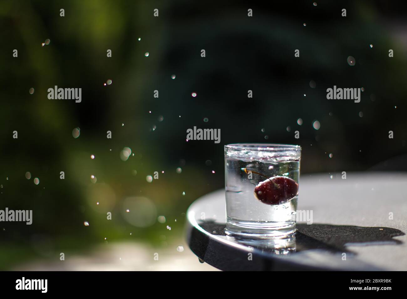 Ciliegia rossa che cade in un bicchiere d'acqua producendo spruzzi d'acqua, congelare nel tempo foto, concettuale. Foto Stock