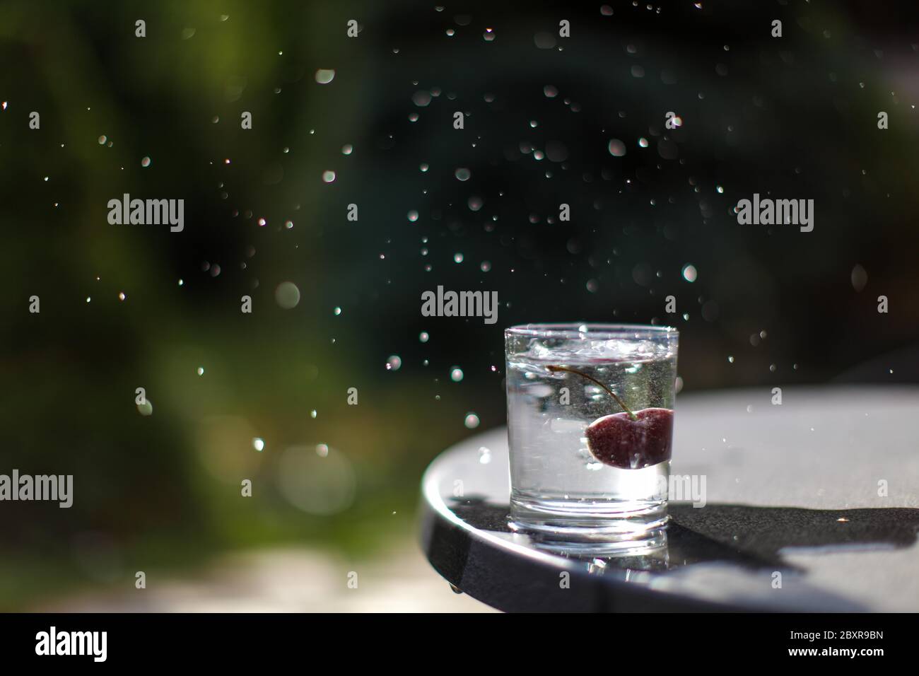 Ciliegia rossa che cade in un bicchiere d'acqua producendo spruzzi d'acqua, congelare nel tempo foto, concettuale. Foto Stock