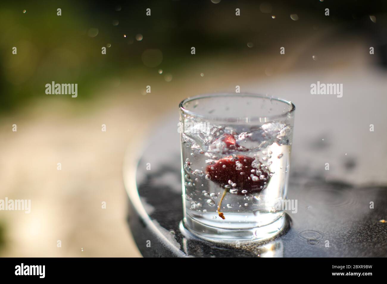 Ciliegia rossa che cade in un bicchiere d'acqua producendo spruzzi d'acqua, congelare nel tempo foto, concettuale. Foto Stock