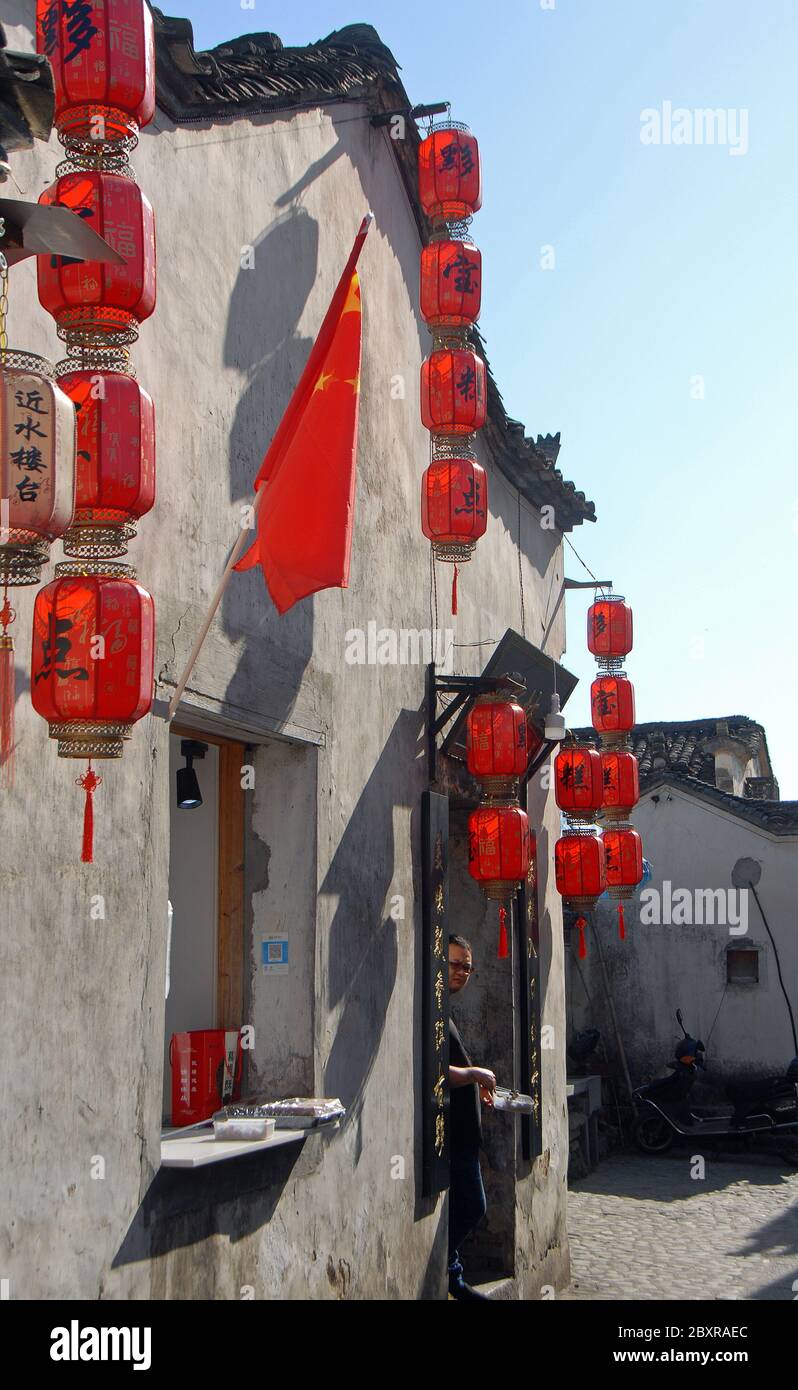 Hongcun Antica Città nella Provincia di Anhui, Cina. Esterno di un edificio tradizionale con lanterne rosse e bandiera cinese ad Hongcun. Negoziante alla porta. Foto Stock