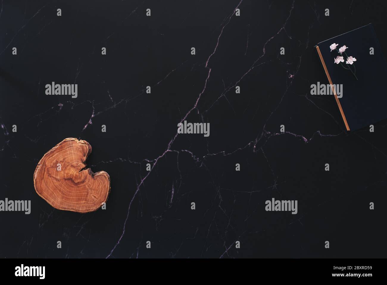 Disposizione piatta di una disposizione floreale e un pezzo di legno e un libro contro marmo nero con abbondanza di spazio di copia Foto Stock