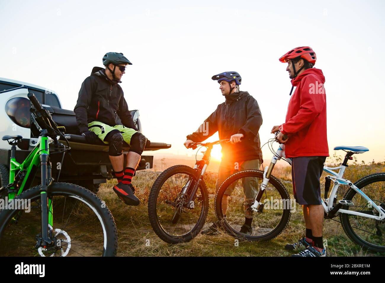 Amici ciclisti riposarsi vicino al pick-up off Road camion dopo Enduro Bike Riding nelle montagne al caldo autunno tramonto. MTB Avventura e viaggio in auto Foto Stock