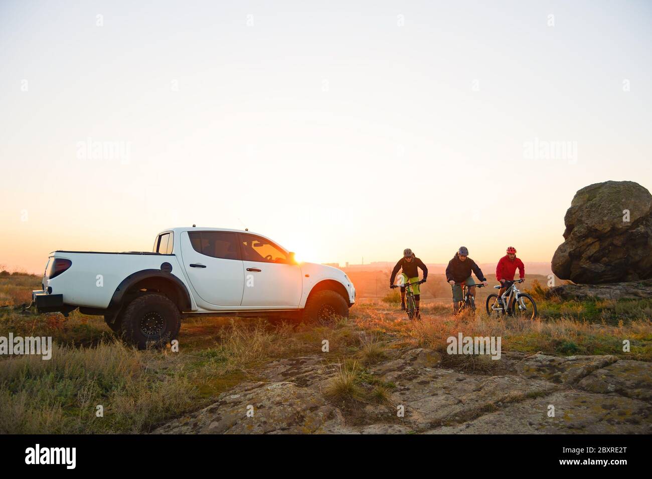 Amici ciclisti Riding Enduro Bikes in the Mountains di fronte al pick-up off Road camion al caldo autunno tramonto. MTB Avventura e viaggio in auto Concep Foto Stock