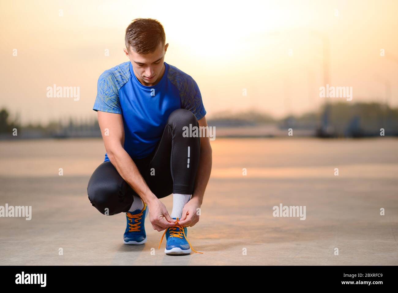 Young Male Sportsman Tying Running Shoes e preparazione per Urban Run al Tramonto. Concetto di stile di vita sano e sport attivo. Foto Stock