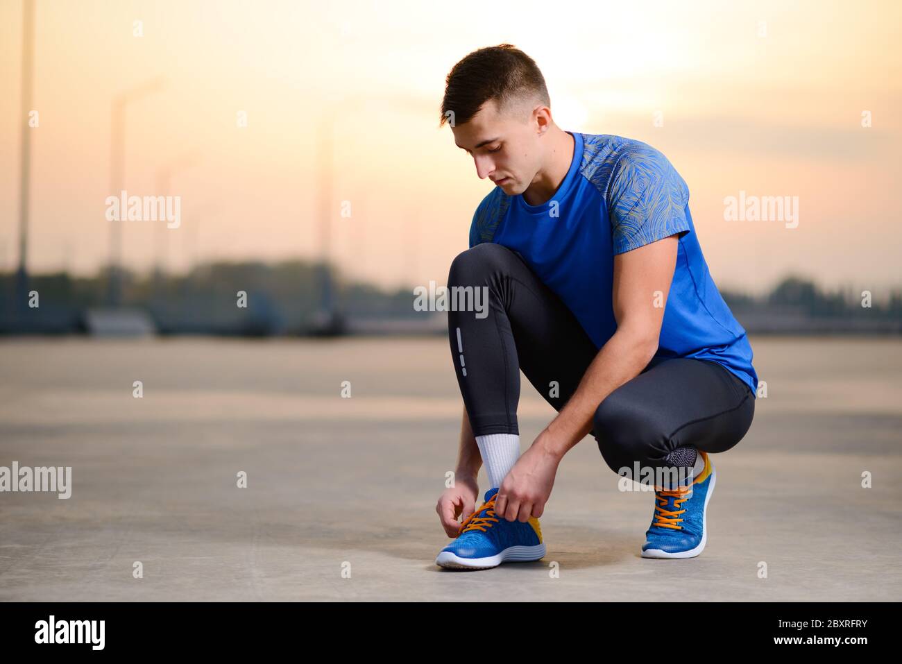 Young Male Sportsman Tying Running Shoes e preparazione per Urban Run al Tramonto. Concetto di stile di vita sano e sport attivo. Foto Stock