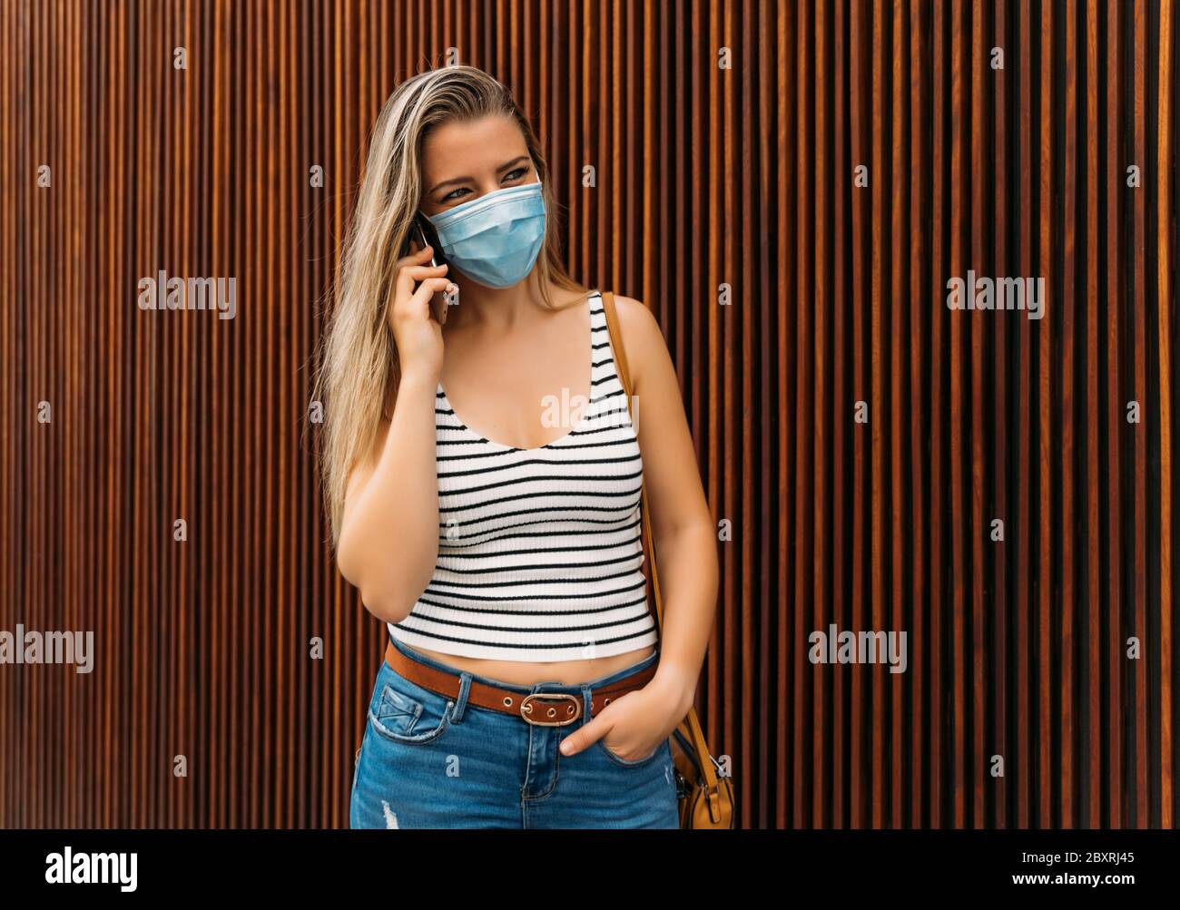 donna in maschera in città utilizzando il suo cellulare durante la pandemia del coronavirus Foto Stock