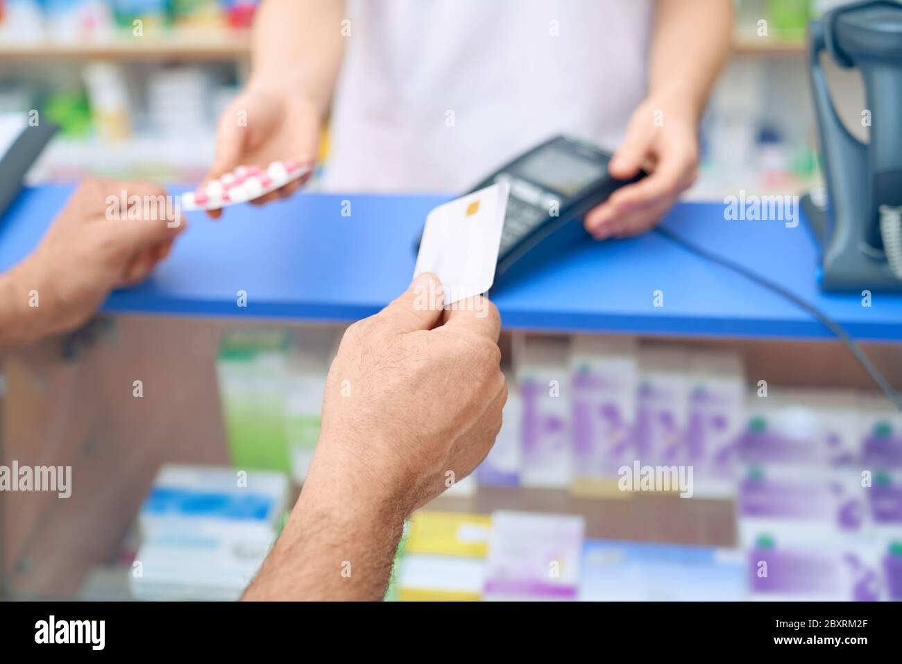 Raccolto di cliente irriconoscibile che effettua il pagamento in farmacia usando la carta di credito. Farmacista terminale di tenuta, uomo che paga per i medicamenti. Macchina di pagamento MODER, confezione Blister di pillole al banco. Foto Stock