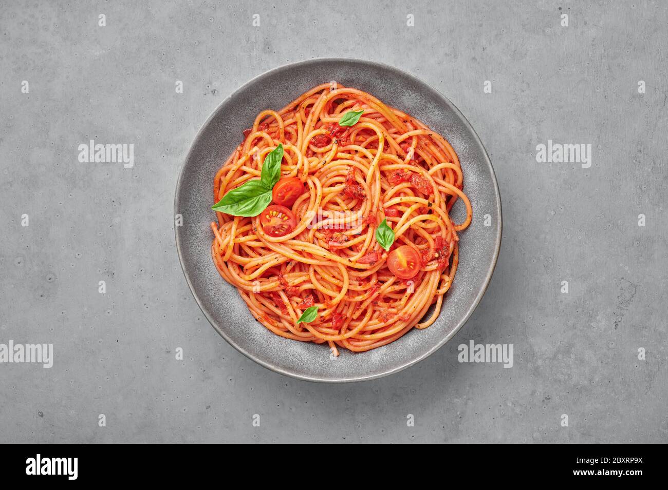Spaghetti di pomodoro in ciotola grigia su fondo di cemento. La pasta con salsa di pomodoro è un piatto classico della cucina italiana. Popolare cucina italiana Foto Stock