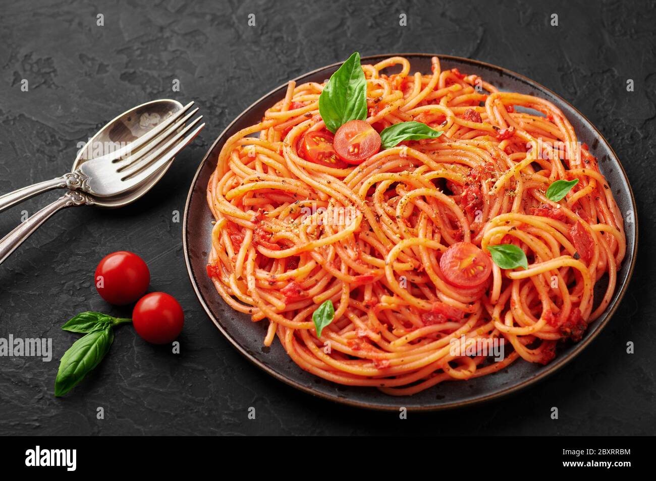 Spaghetti di pomodoro su piatto nero su sfondo di ardesia scuro. La pasta con salsa di pomodoro è un piatto classico della cucina italiana. Popolare cucina italiana Foto Stock