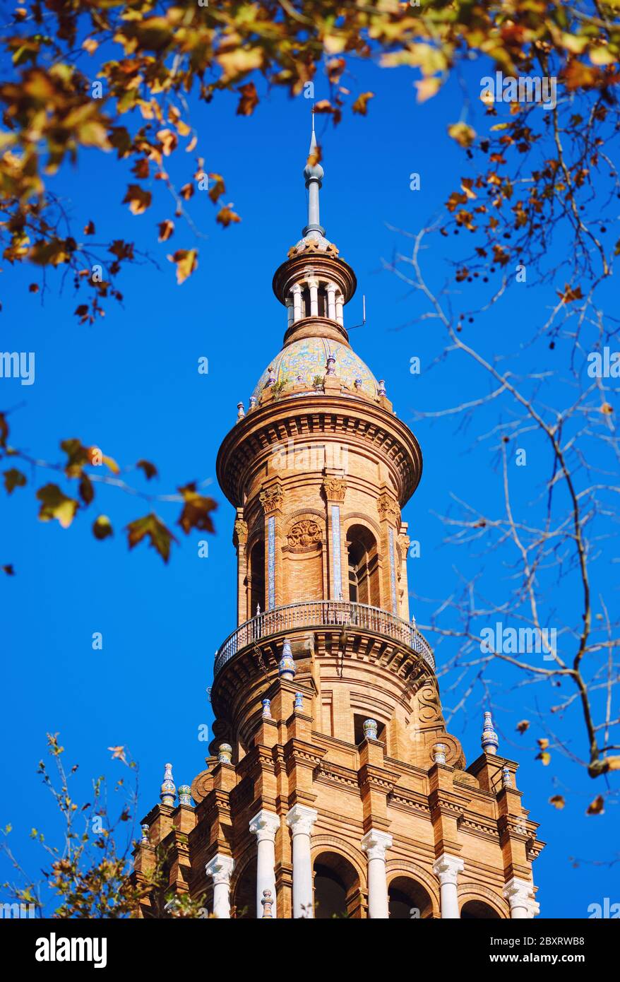 Architettura antica vista torre in Plaza de España contro il cielo blu soleggiato e chiaro incorniciato da foglie di albero. Punto di riferimento principale luogo popolare per i turisti, trave Foto Stock