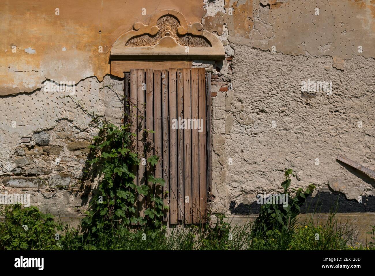 Stagionato e sbucciato dalla facciata di una casa padronale abbandonata. Finestra coperta da lacci di legno. Jablonica, Slovacchia. Foto Stock
