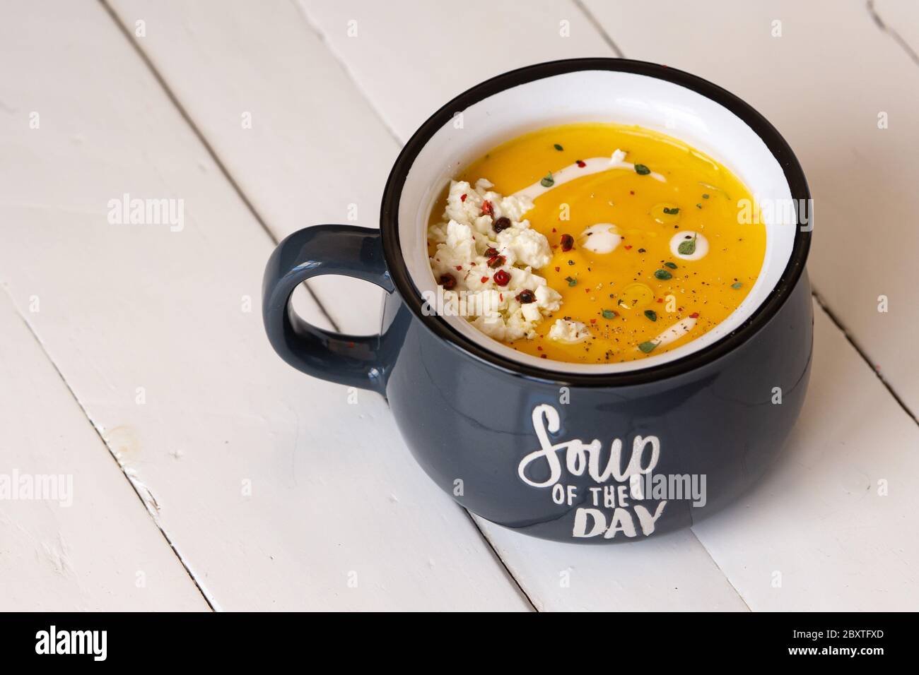 Zuppa di zucca in una ciotola blu isolata. Iscrizione: Zuppa del giorno. Pranzo o cena vegetariani. Concetto di cibo sano. Spazio di copia. Foto Stock
