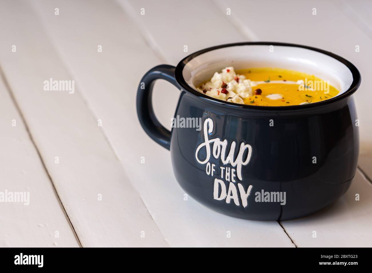 Zuppa di zucca in una ciotola blu isolata. Iscrizione: Zuppa del giorno. Pranzo o cena vegetariani. Concetto di cibo sano. Spazio di copia. Foto Stock