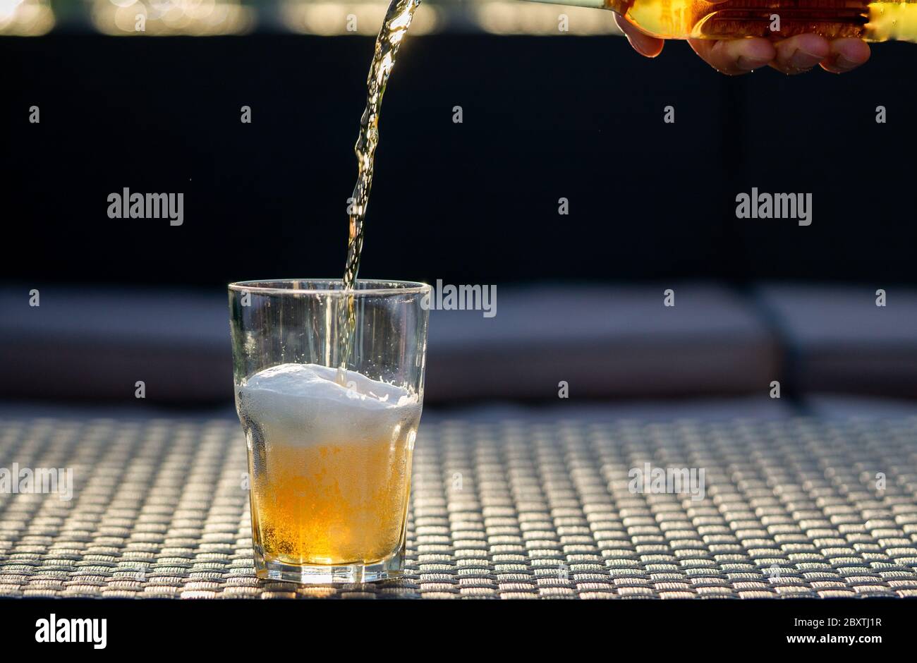 Porta a mano una bottiglia di birra. Birra che cade al bicchiere. Movimento di congelamento. Bar, pub, ristorante. Spazio di copia, sfondo grigio. Foto Stock