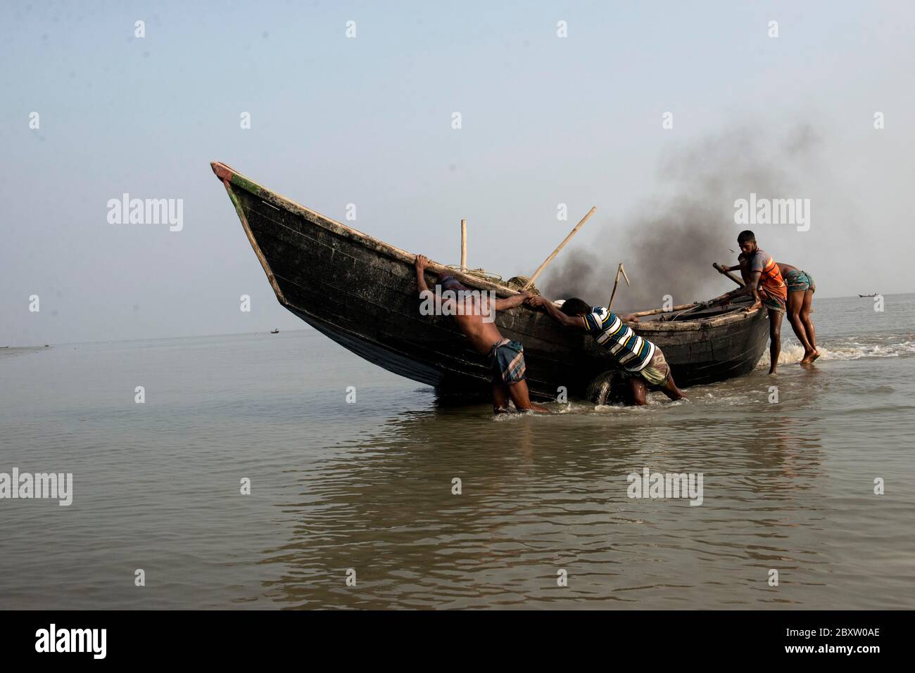 I pescatori tornano dal mare con pesce e stanno cercando di mantenere la loro barca in un luogo sicuro oltre la spiaggia di mare. Foto Stock