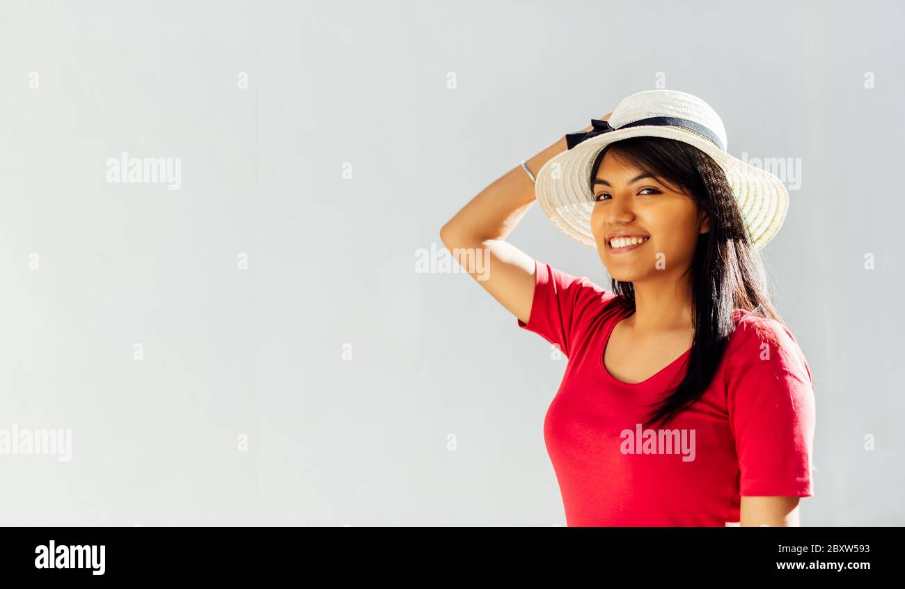 Donna latina brunette in profilo che tiene un cappello con una mano sulla testa e sorridente. Spazio di copia Foto Stock