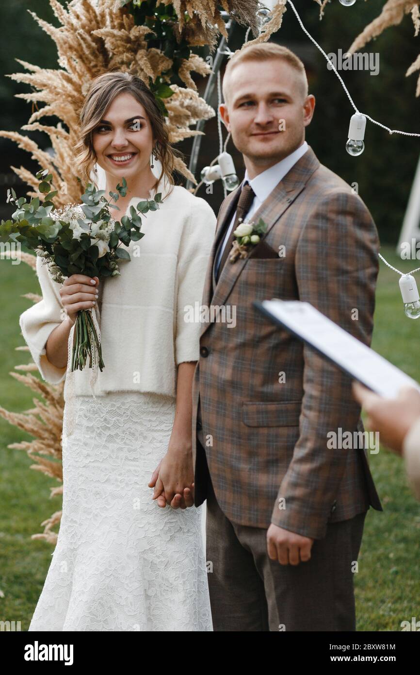 Felice neqr in piedi newlywed l'arco di nozze e tenersi le mani l'un l'altro. Sposa e sposo. Cerimonia nuziale. Foto Stock
