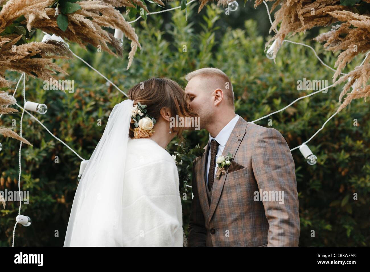 Sposa e sposo baciando sullo sfondo dell'arco di nozze. Sposa e sposo. Cerimonia nuziale. Foto Stock