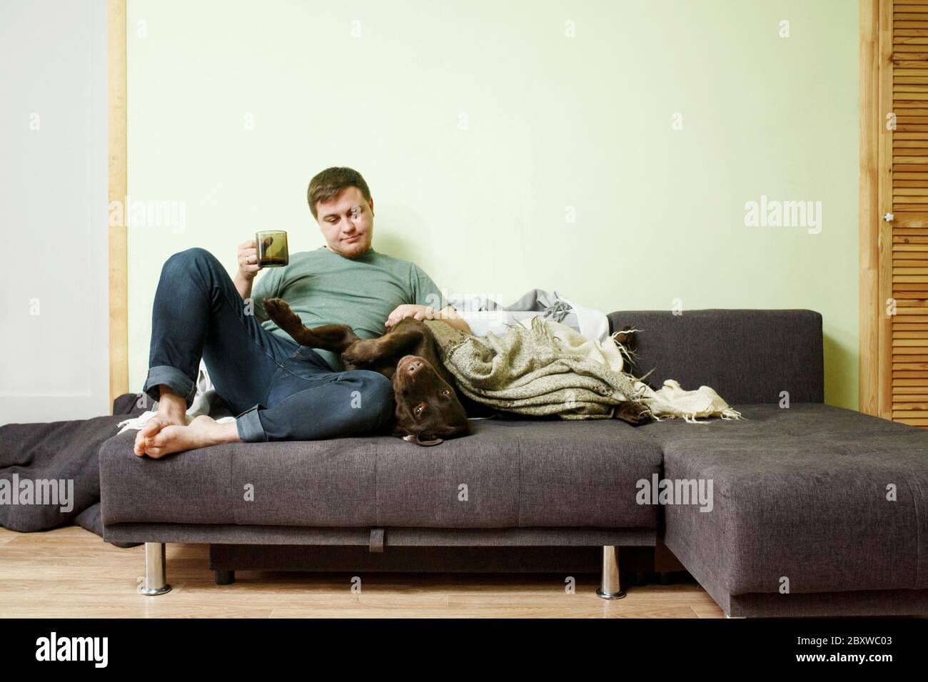 Felice uomo bello seduto sul divano a casa con cane labrador Retriever che si trova sulle ginocchia, cane canino terapia concetto Foto Stock