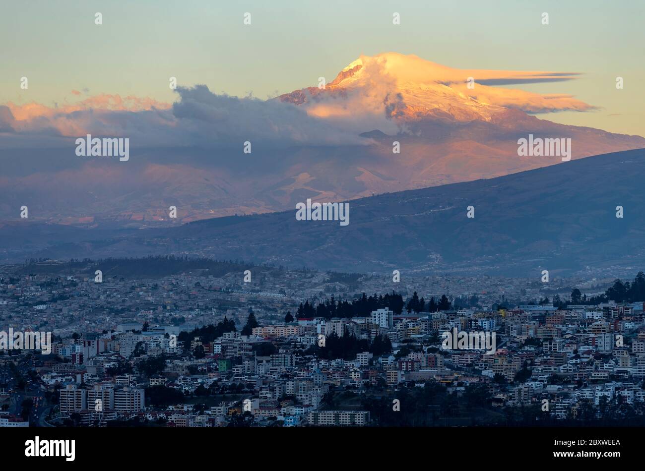 Suggestivo paesaggio del vulcano Cayambe al tramonto con lo skyline della città di Quito, Ecuador. Foto Stock