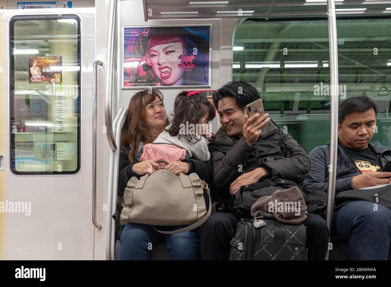 I genitori con il loro bambino che fanno un giro in treno a casa e usano il loro smartphone per intrattenere il bambino, a Tokyo Giappone. Foto Stock