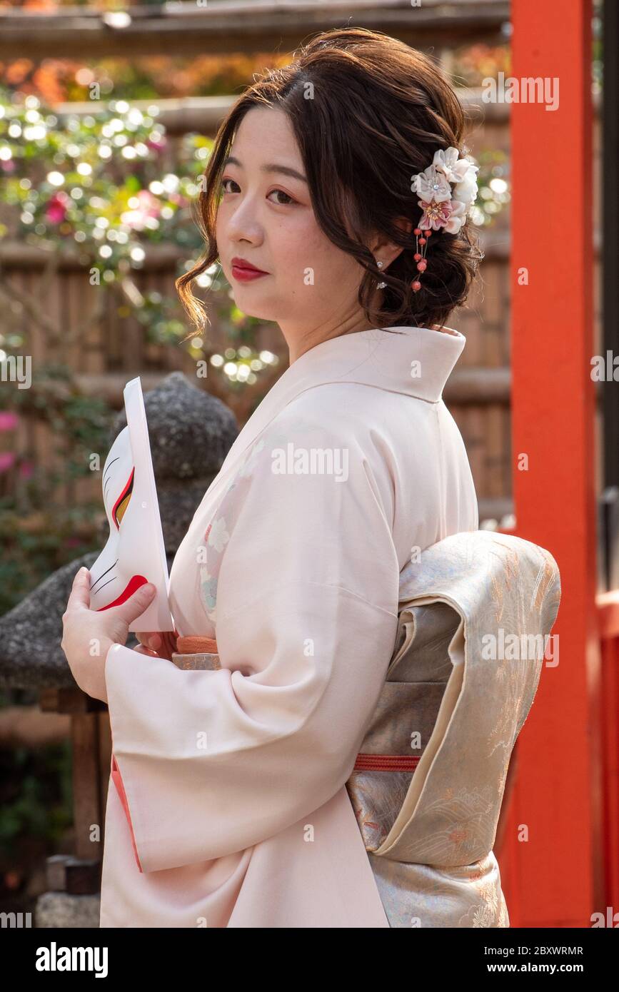 Teen giapponese che indossa kimono tradizionale è in posa con una maschera kitsune. Maschera di volpe giapponese. Queste maschere sono indossate per divertimento, in festival e onorare gli dei Foto Stock