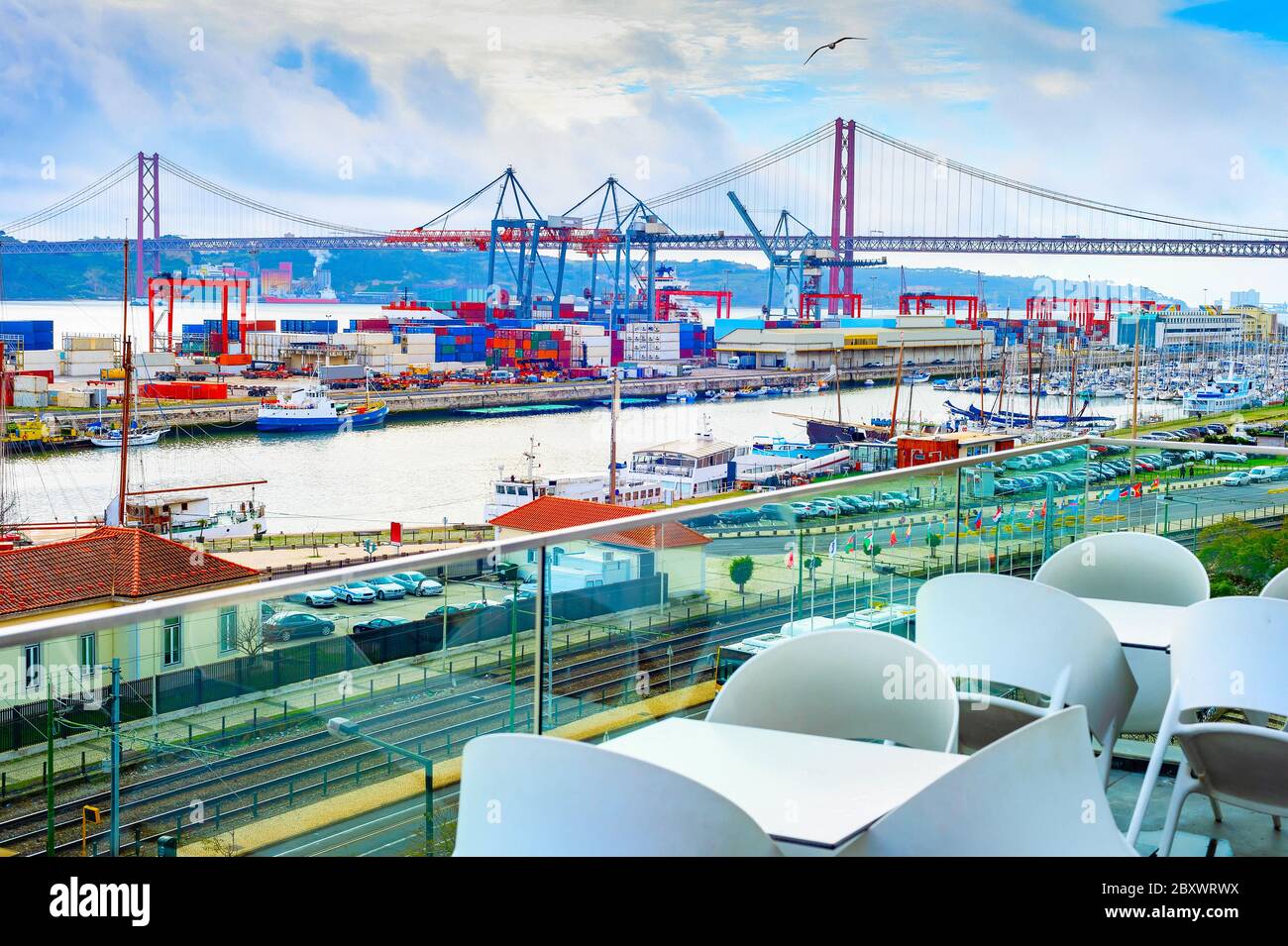 Vista porto commerciale di Lisbona dalla terrazza ristorante all'aperto, container, gru merci, motoscafi, binari ferroviari e parcheggio auto, ponte 25 aprile Foto Stock