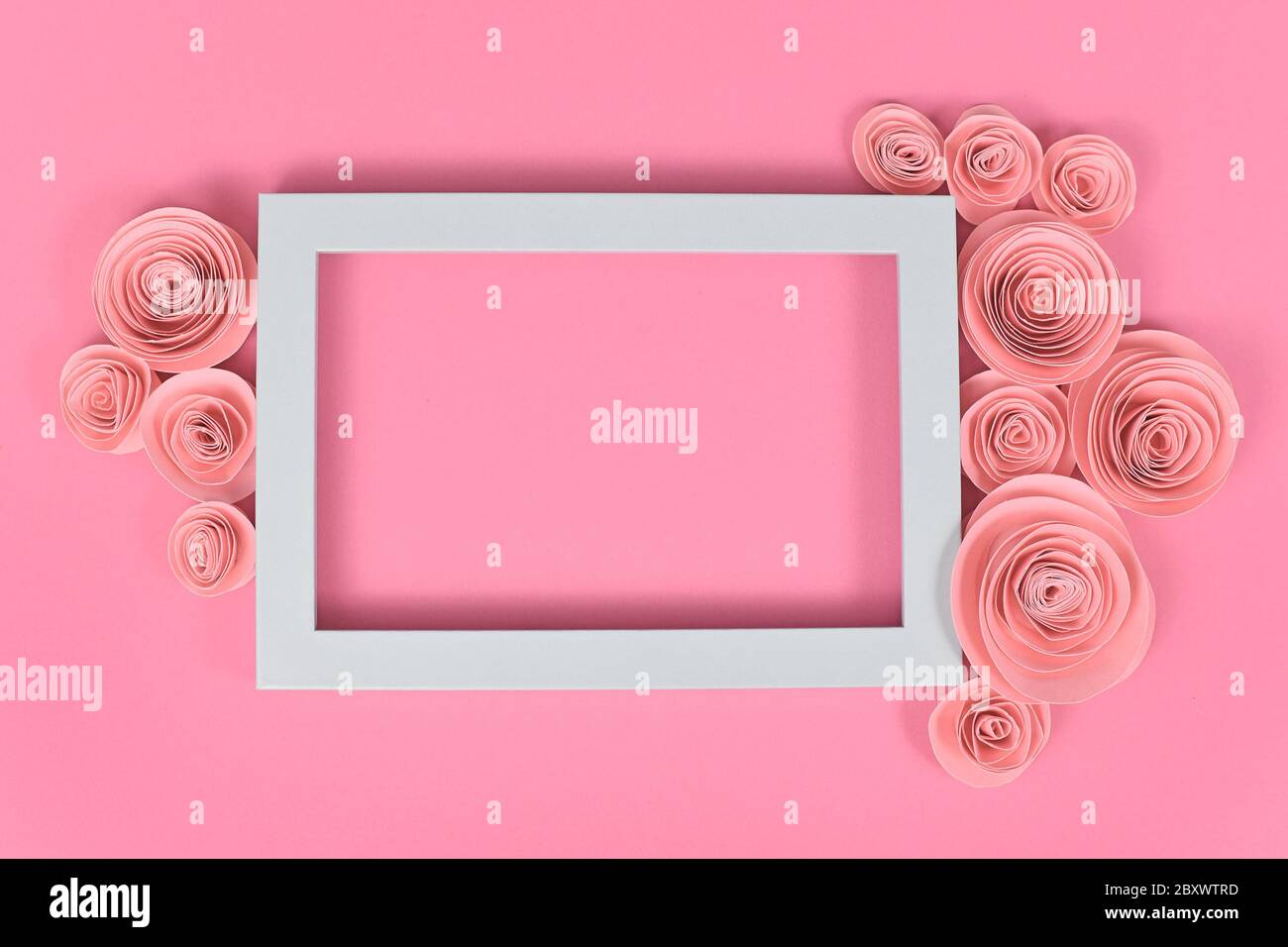 Fiore piatto con cornice vuota circondata da romantiche rose artigianali di carta su sfondo rosa pastello Foto Stock