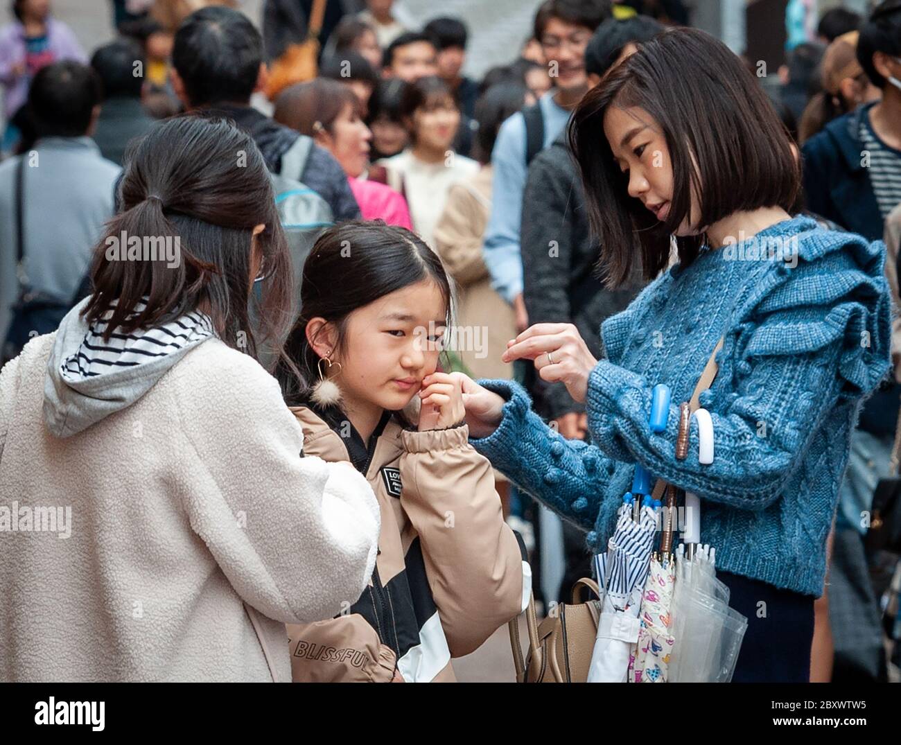 Due ragazzi giapponesi aiutano il loro amico a montare gli orecchini appena acquistati a Takeshita Street, il centro di moda nel distretto di Harajuku a Tokyo, Giappone. Foto Stock