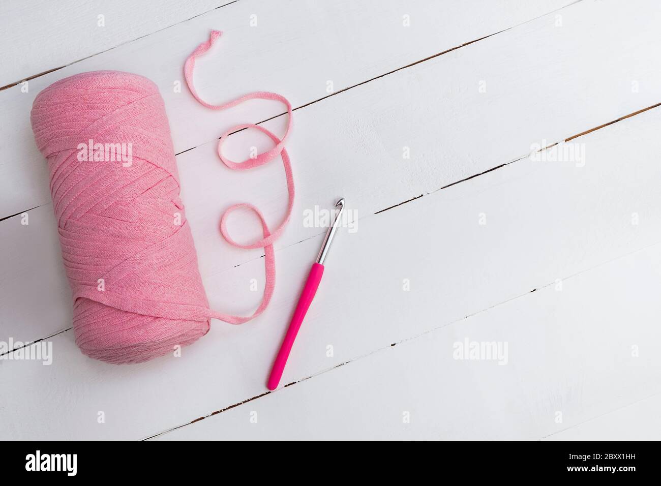 Vista dall'alto del filo rosa con uncino su tavolo di legno bianco con spazio per il testo. Fatti a mano e fai da te Foto Stock