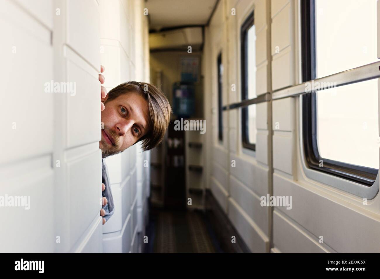 Ritratto di un uomo allegro sulla barba in treno. Guardando la macchina fotografica. Curioso compagno di viaggio da un compartimento vicino sul treno. Incontro durante il viaggio Foto Stock