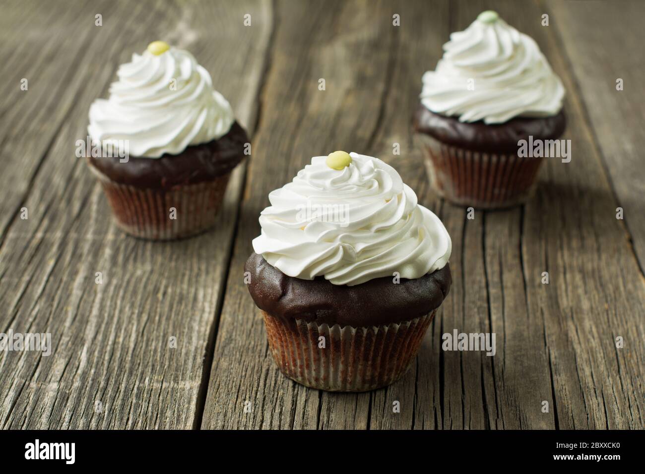 Cupcake di cioccolato fatti in casa in fodere di cupcake, sormontata con panna montata, decorata con caramelle a forma di bottoni, sullo sfondo rustico della tavola di legno. Foto Stock