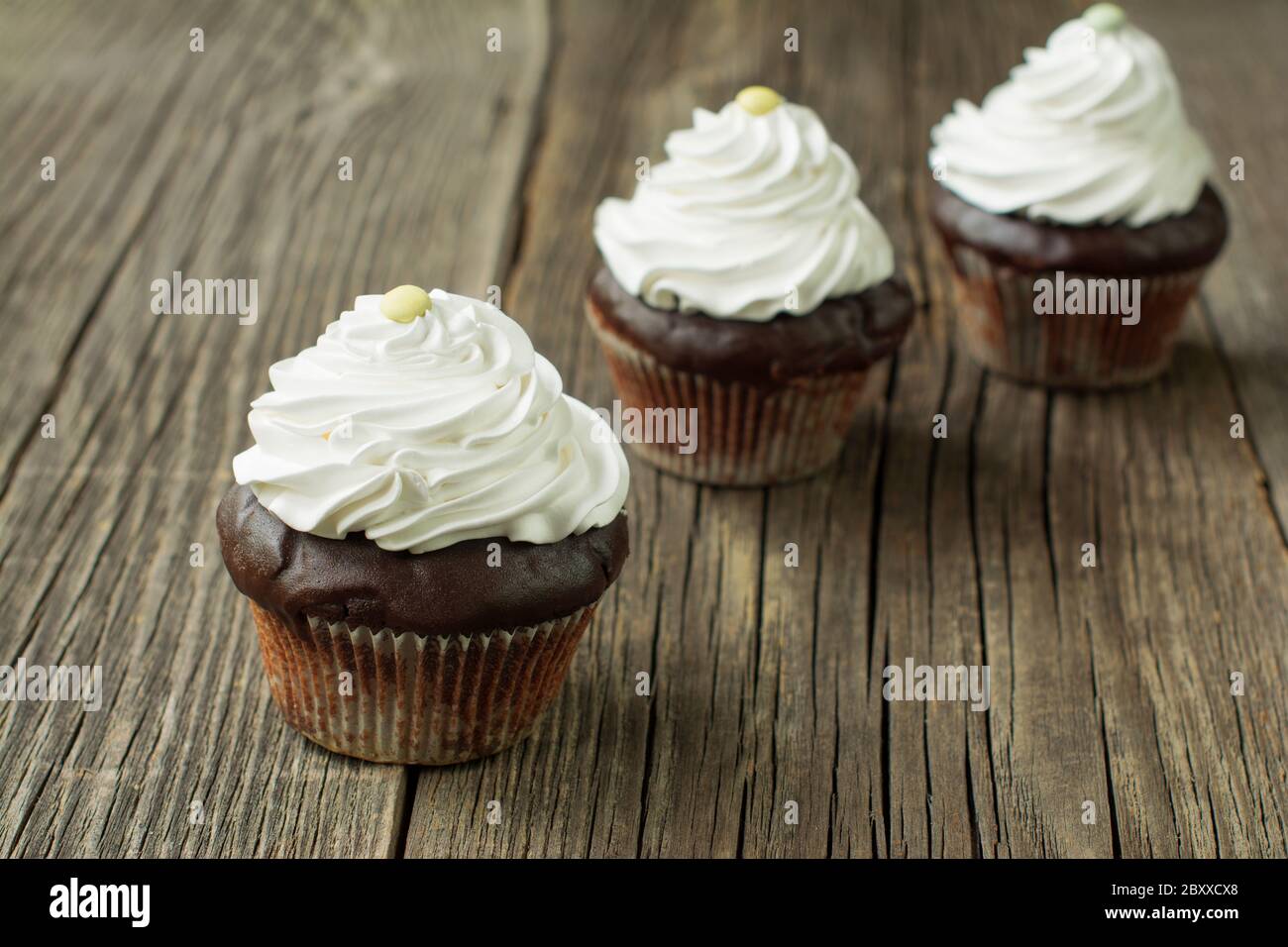 Cupcake al cioccolato in cartoni di carta, sormontati con panna montata e decorati con caramelle a forma di bottoni, sulle tavole rustiche in legno. Foto Stock