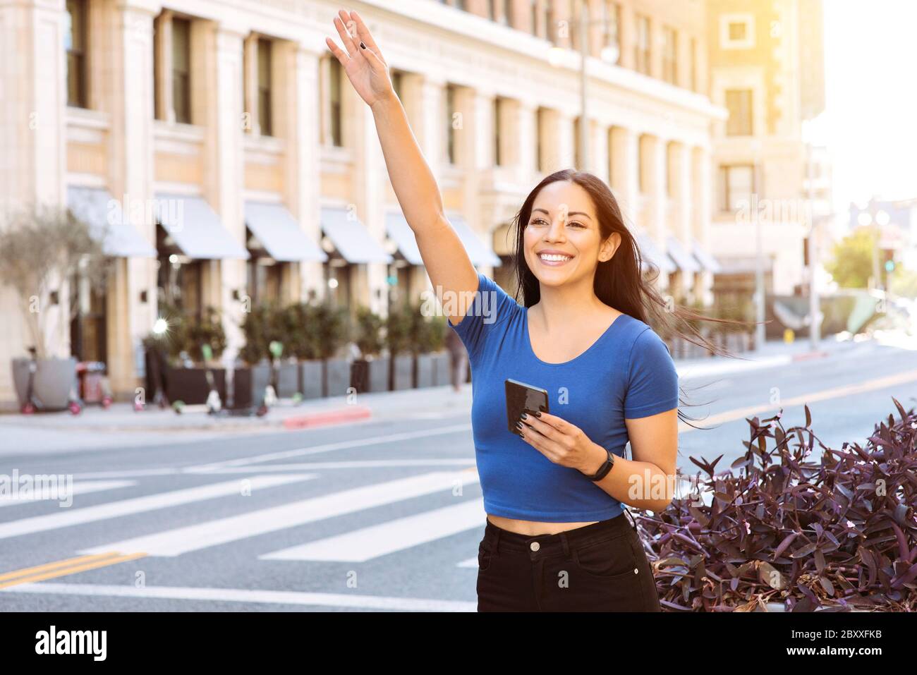 Giovane donna di colore ondeggia la sua mano per chiamare una parte di corsa nella città - Uber - Lyft - Daytime Foto Stock