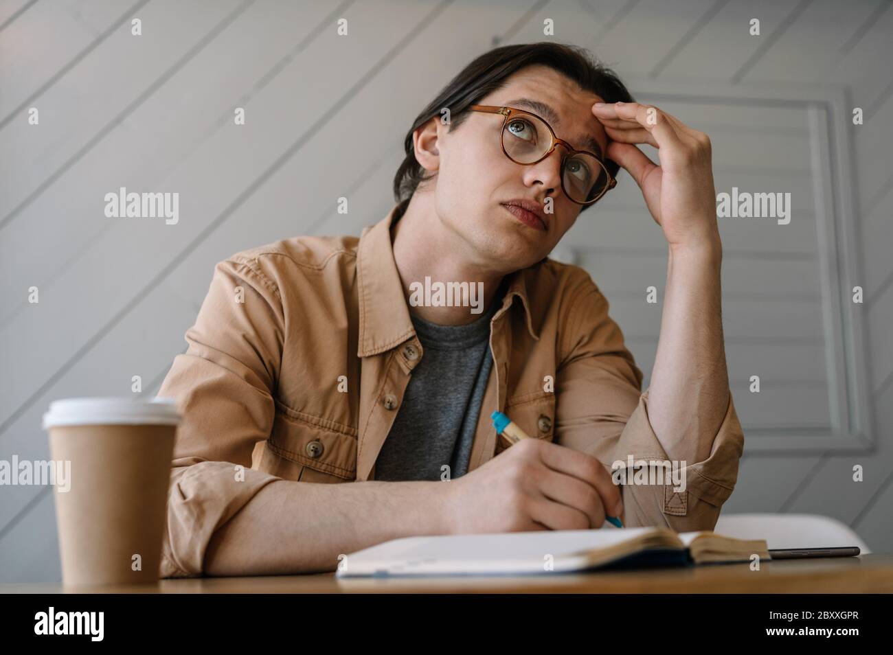 Uomo stanco e impegnato alla ricerca di soluzioni creative, idee, brainstorming sul posto di lavoro. Hipster pensivo in occhiali di stile lavorando progetto freelance Foto Stock